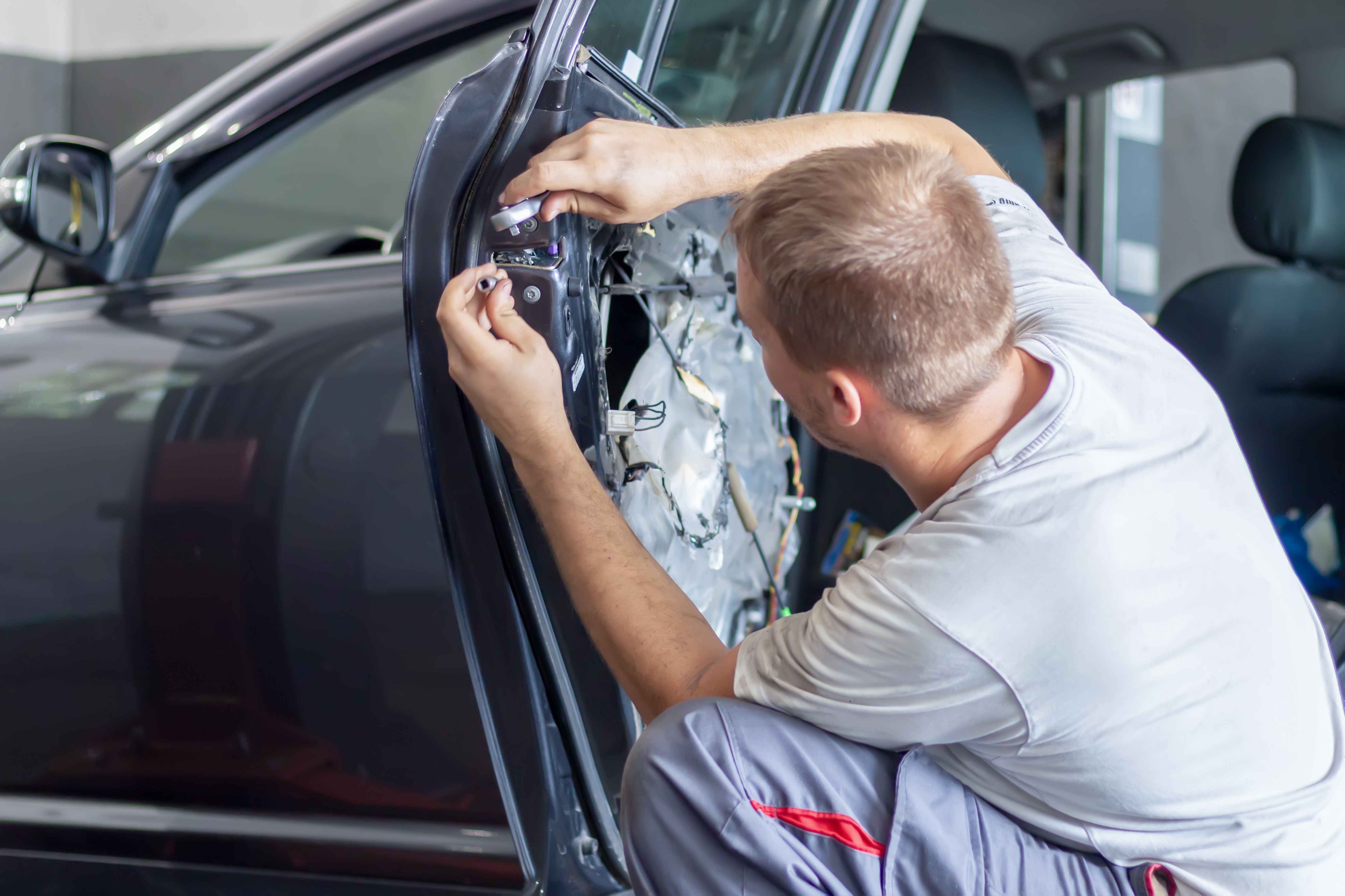 Car mechanic trying to fix vehicle door lock. The concept car door repairing services and doors lock repair.